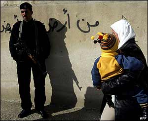 Palestinian woman with her baby on her way to vote walks by Palestinian policemen in the West Bank town of Abu Dis