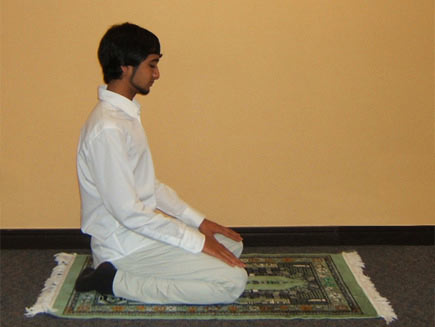 A man sits on his heels with his hands on his thighs, his head facing forwards and down