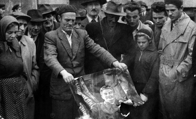 A man, surrounded by a crowd, burns a picture of Stalin. (Photo: Jack Esten/Getty Images)