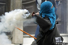 A masked student throws a tear gas canister