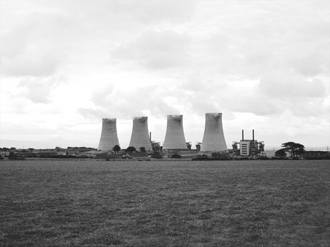 Black and white view across fields to a power station. The view is dominated by four large cooling towers.