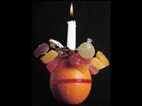 A Christingle - an orange with a candle pushed into the centre of the orange, a red ribbon around the outside, and sweets or dried fruits stuck into the orange with cocktail sticks